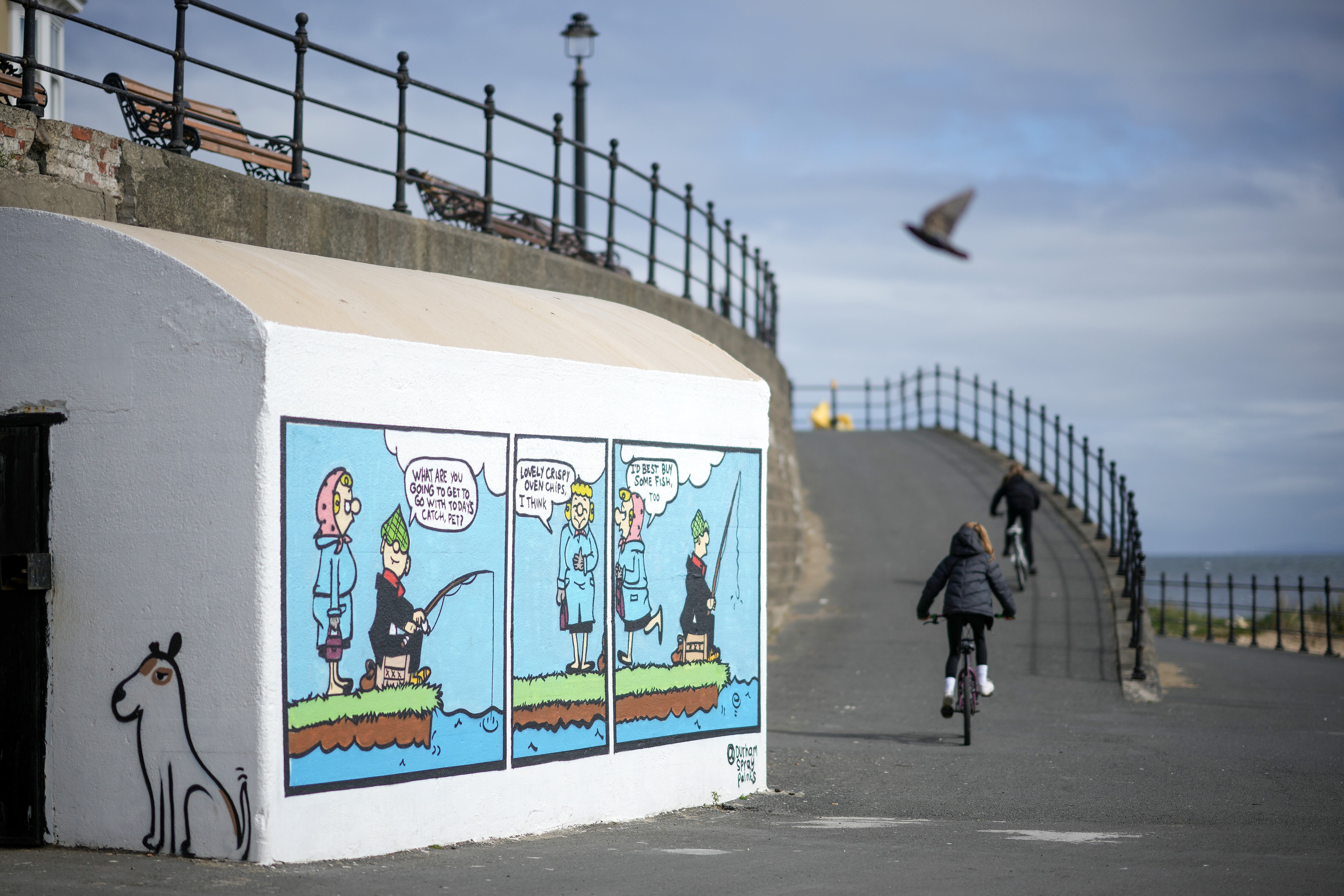 HARTLEPOOL, ENGLAND - APRIL 27: Children ride their bikes past a wall mural of the working class cartoon character Andy Capp, created by local cartoonist Reg Smythe, in the Headland area of Hartlepool on April 27, 2022 in Hartlepool, England. A third of the Hartlepool Borough Council's seats are in play on May 5, which could upend the current coalition of Tories and independents that has governed since Labour lost control in 2019. The council is returning to an "election by thirds" system following last year's whole-council contest, which was prompted by changes to the borough's electoral boundaries. (Photo by Christopher Furlong / Getty Images)