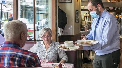 An employee wears a face mask to serve meals to customers during lunch time at the 'La Fontaine de Mars' restaurant in Paris.