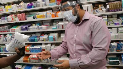 (FILES) In this file photo taken on April 17, 2020 A pharmacist at a Boots Pharmacy, in PPE including a full face mask as a precautionary measure against COVID-19, passes a completed prescription to Bikeworks cycling instructor Jelil Adebiyi (L), for him to to deliver to vulnerable people as part of the Bikeworks Cycle Delivery Service (COVID-19) in east London on April 17, 2020. - British pharmacies Boots are launching a new service in 14 UK cities, including London and Edinburgh, to deliver medicines and cosmetics by courier with the Deliveroo platform. (Photo by ISABEL INFANTES / AFP)