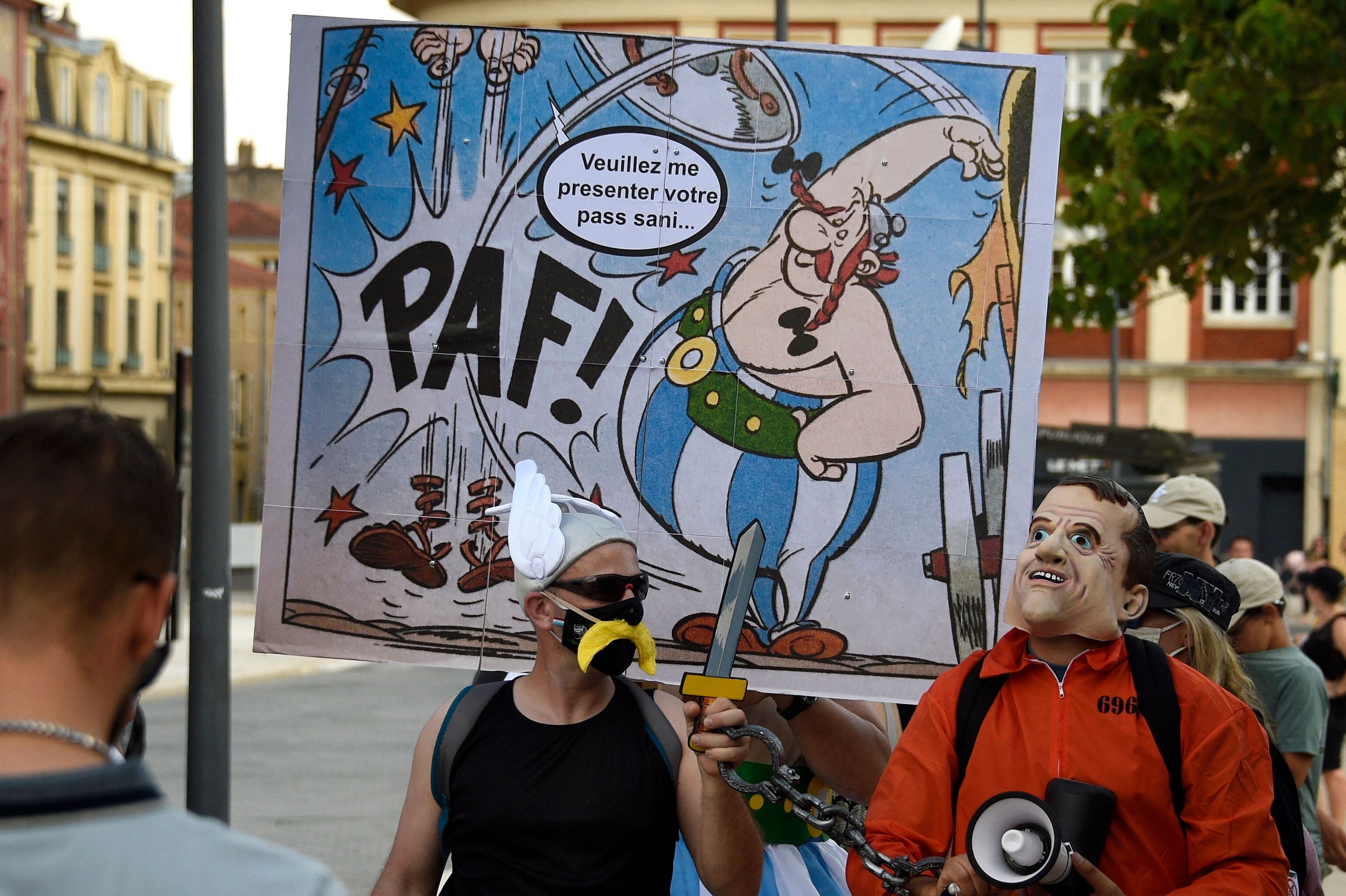 A protester holds a placard depicting French cartoon character Obelix that reads 'please show me your sanitary pass' as he takes part in a national day of protest against the compulsory Covid-19 vaccination for certain workers and the compulsory use of the health pass called for by the French government in Metz on August 14, 2021. (Photo by JEAN-CHRISTOPHE VERHAEGEN / AFP)