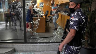 A Lebanese policeman stands guard next to a bank window that was broken by depositors to exit the bank after attacking it trying to get blocked money. A Lebanese activist group said they will continue to organize bank raids to help people retrieve their trapped savings. AP