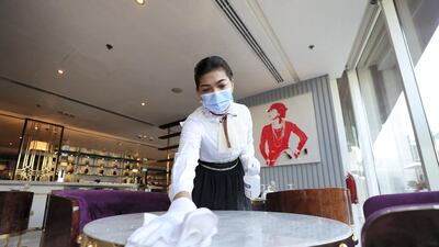 An employee disinfects a table at a cafe in Dubai. Chris Whiteoak / The National