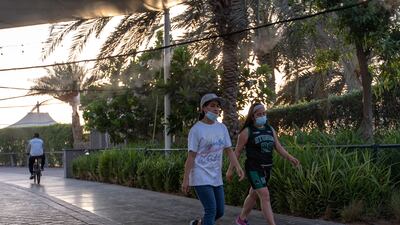 Abu Dhabi residents walk along the Corniche where a misting system is attached along the walkway to help beat the heat and humidity this summer on June 26, 2021. Victor Besa / The National.